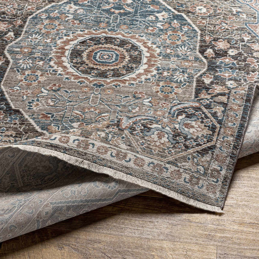 Close-up of the Baychester Brown Area Rug showing its traditional oriental design, denim blue, brown, and sage colors, and soft texture. Fold