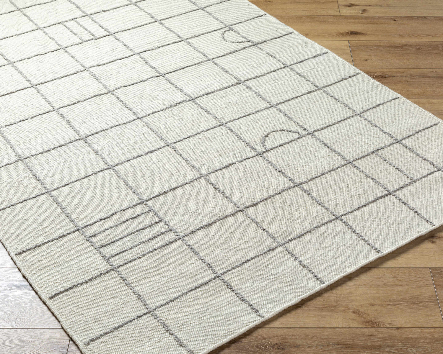 Close-up of Tieve Black & White Grid Wool Rug showing cream color and gray grid pattern on wood floor. Corner