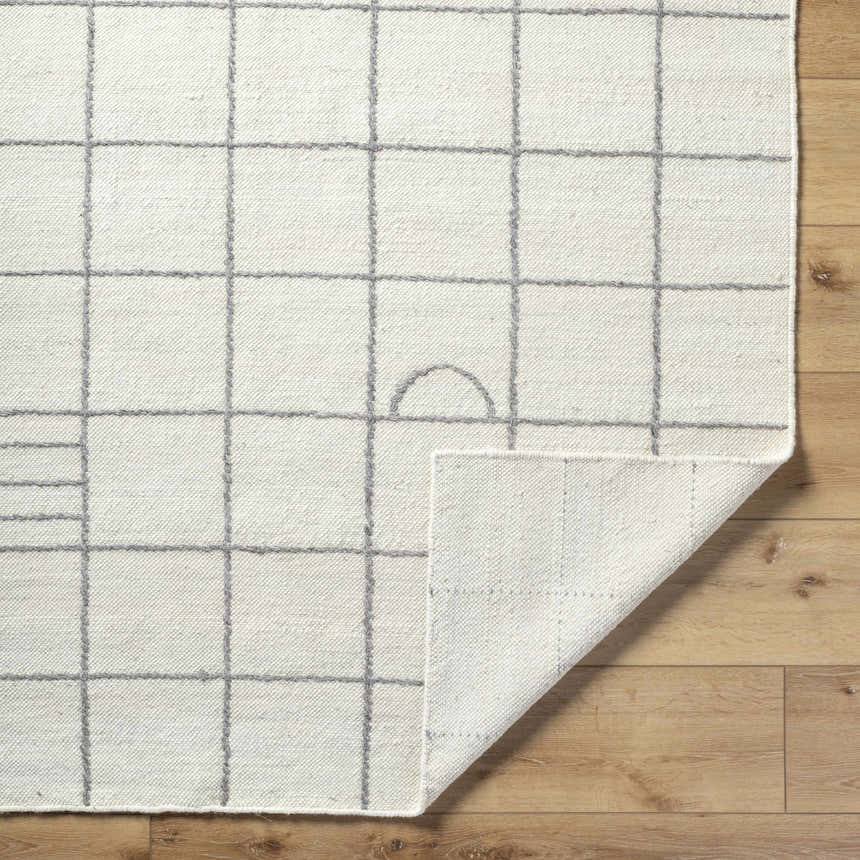 Close-up of the Tieve Black & White Grid Wool Rug showing cream color and gray grid pattern. Hand woven texture detail. Fold