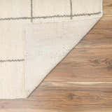 Close-up of Tieve Black & White Grid Wool Rug showing cream wool texture and gray grid pattern on wood floor. Fold