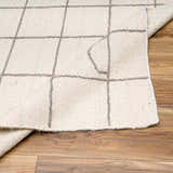 Close-up of Tieve Black & White Grid Wool Rug showing cream color and gray grid pattern on wood floor. Fold