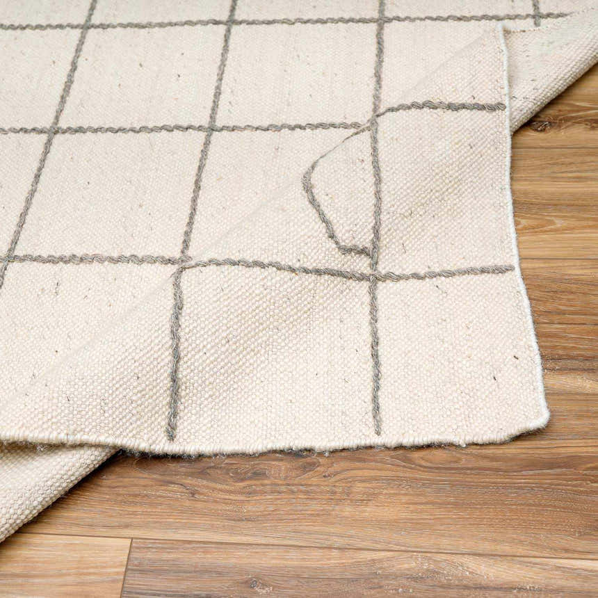 Close-up of Tieve Black & White Grid Wool Rug showing cream color and gray grid pattern on wood floor. Fold