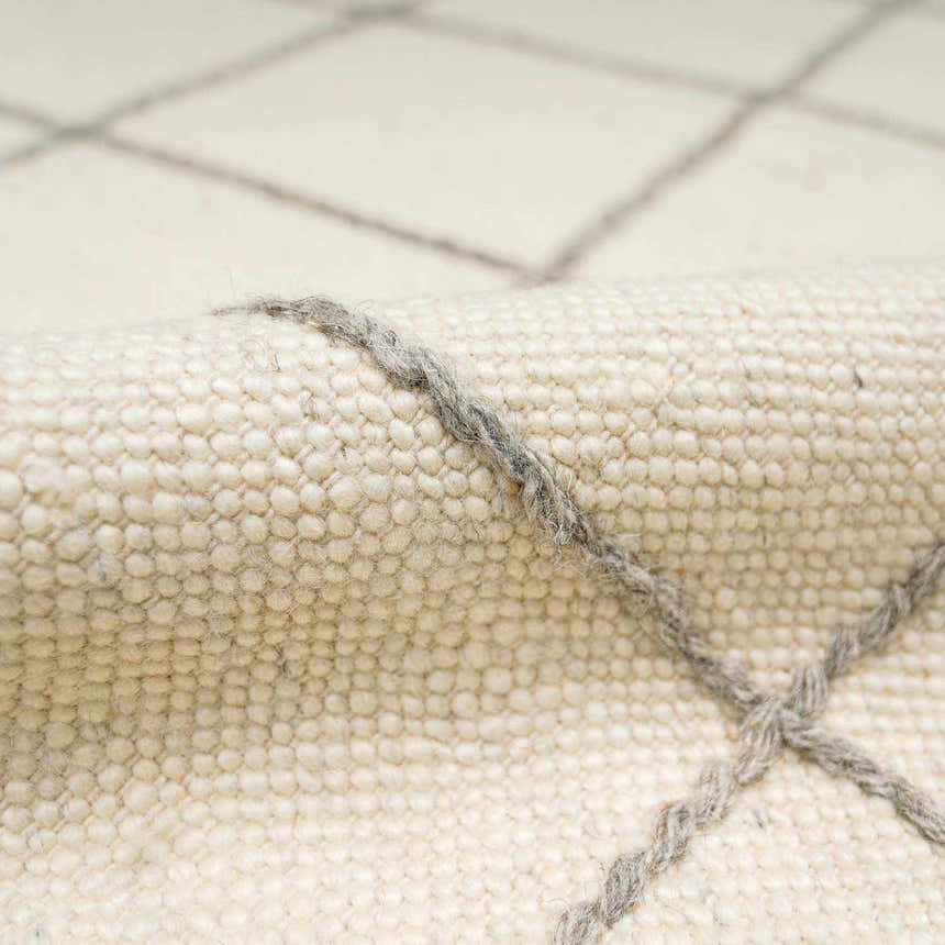 Close-up of the Tieve Black & White Grid Wool Rug showing cream wool texture and gray woven grid pattern. Fold