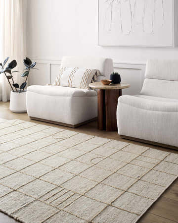 Living room scene with beige Tieve Area Rug, two white armchairs, and a wood side table. Modern, neutral aesthetic. Roomscene-Rectangle