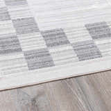 Close-up of the Azrika Gray Checkered Washable Rug showing the beige, gray, and light gray geometric pattern. Corner