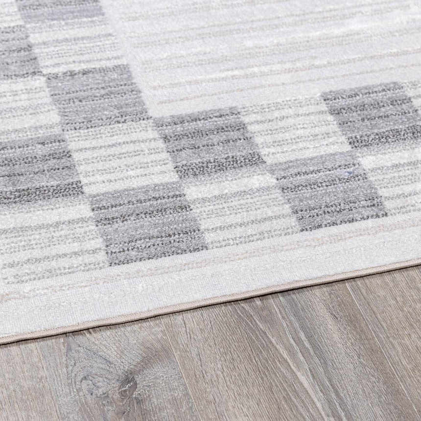Close-up of the Azrika Gray Checkered Washable Rug showing the beige, gray, and light gray geometric pattern. Corner