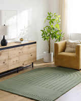 Living room scene with a green Arnona Area Rug, wood cabinet, tan chair, and potted plant. Roomscene-Custom