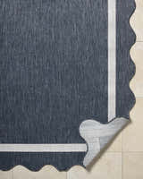 Close-up of the Varro Navy Area Rug showing its navy color, cream border, wavy edge, and polypropylene texture. Fold