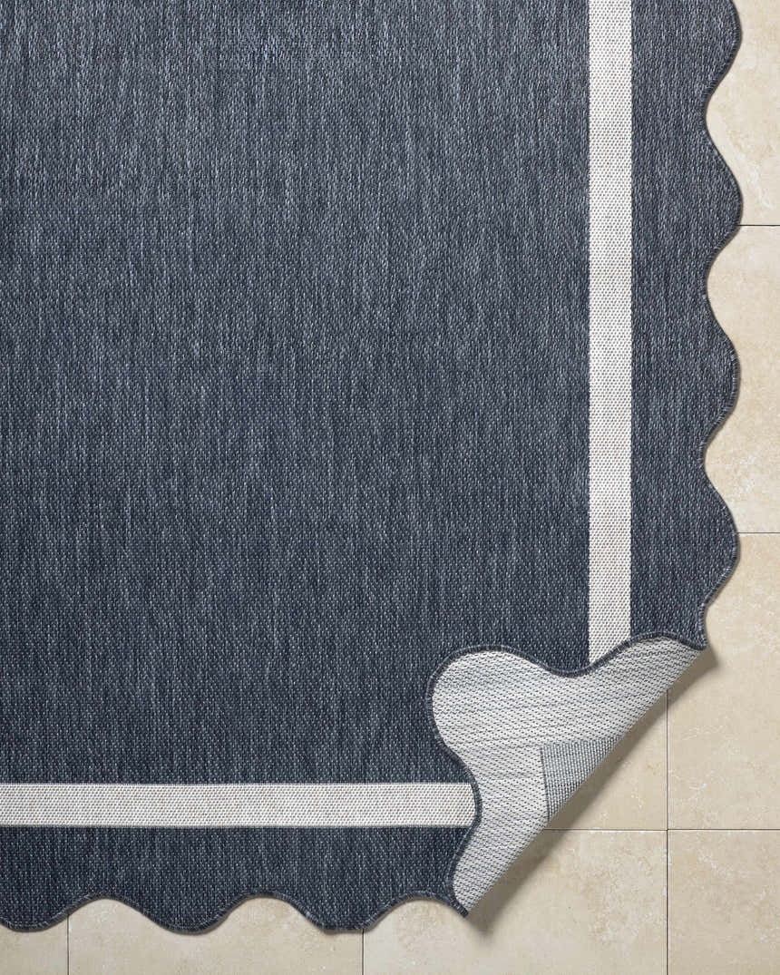 Close-up of the Varro Navy Area Rug showing its navy color, cream border, wavy edge, and polypropylene texture. Fold