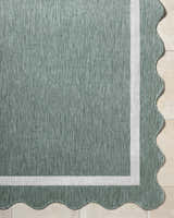 Close-up of the Varro Medium Green Area Rug showing texture, cream border, and scalloped edge. Corner