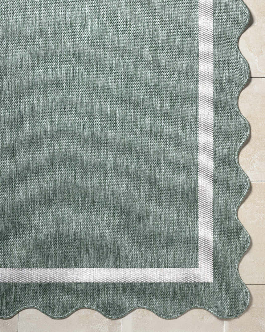 Close-up of the Varro Medium Green Area Rug showing texture, cream border, and scalloped edge. Corner