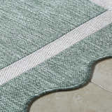Close-up of the woven texture of the Varro Medium Green Area Rug, with cream stripe and scalloped edge. Texture