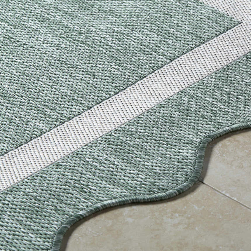 Close-up of the woven texture of the Varro Medium Green Area Rug, with cream stripe and scalloped edge. Texture