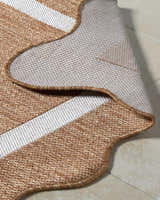 Close-up of the machine woven Varro Rust Area Rug showing cream stripes, rust color, and backing. Fold