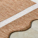 Close-up of Varro Rust Area Rug showing cream stripe, rust weave texture, and scalloped edge detail on tile flooring. Texture