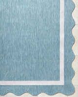 Close up of the Varro Aqua Area Rug showing its aqua color, white border, and scalloped edge. Corner