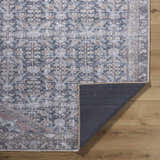 Close-up of the Valar Washable Area Rug. Beige, black, and blue traditional pattern. Machine woven polyester rug on wood floor. Fold