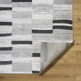 Close-up of the Vasso Gray Area Rug showing its ink, light silver, and gray geometric pattern and machine-woven texture. Fold