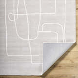 Close-up of Vatsa Gray Abstract Area Rug. Light silver wool rug with a geometric line design on a wood floor. Fold
