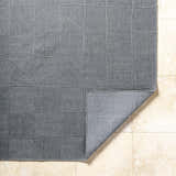 Close-up of the Veras Charcoal Area Rug showing a geometric block pattern and textured weave on a beige tile floor. Fold
