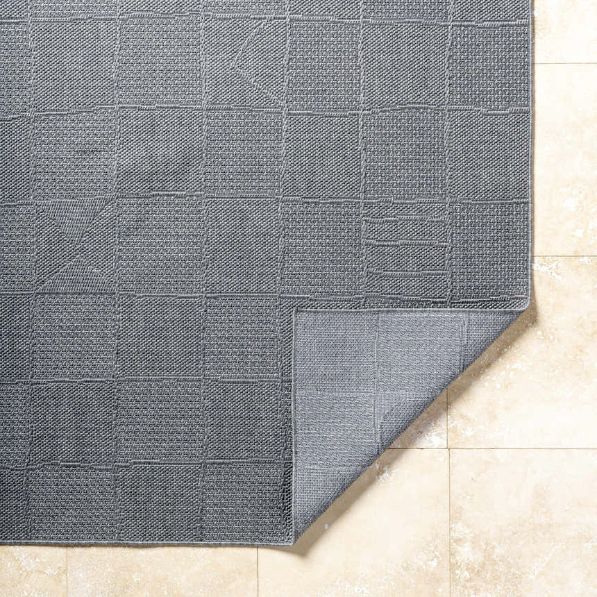 Close-up of the Veras Charcoal Area Rug showing a geometric block pattern and textured weave on a beige tile floor. Fold