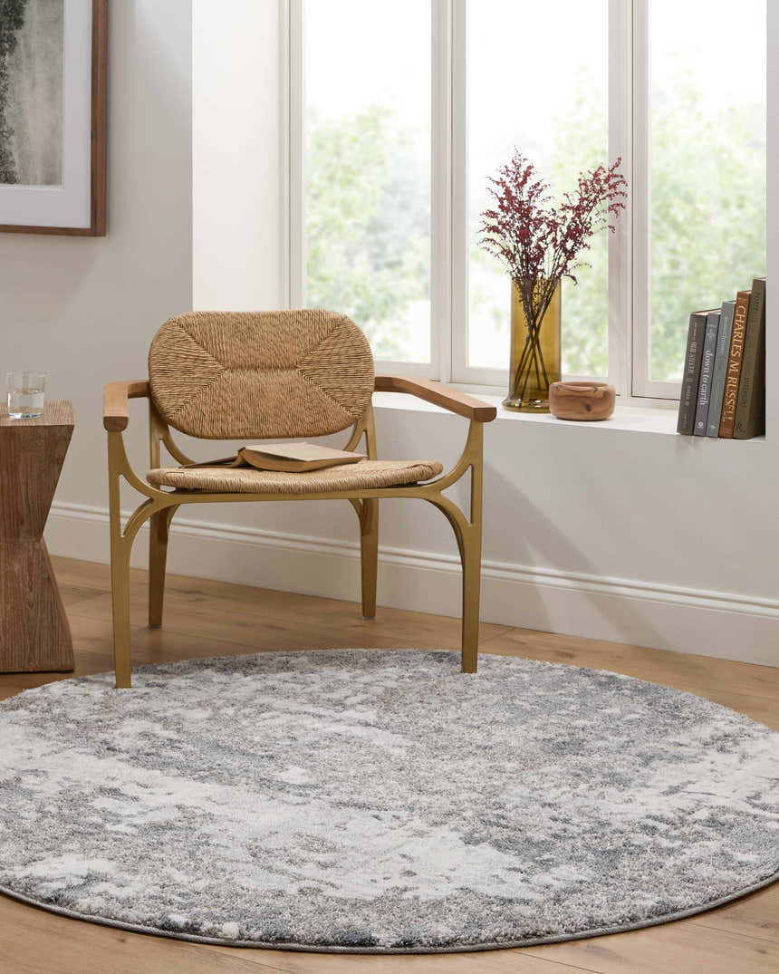 Light-filled room with round Walhonding Area Rug in denim, ivory, and gray under a woven chair by a window. Roomscene-Round