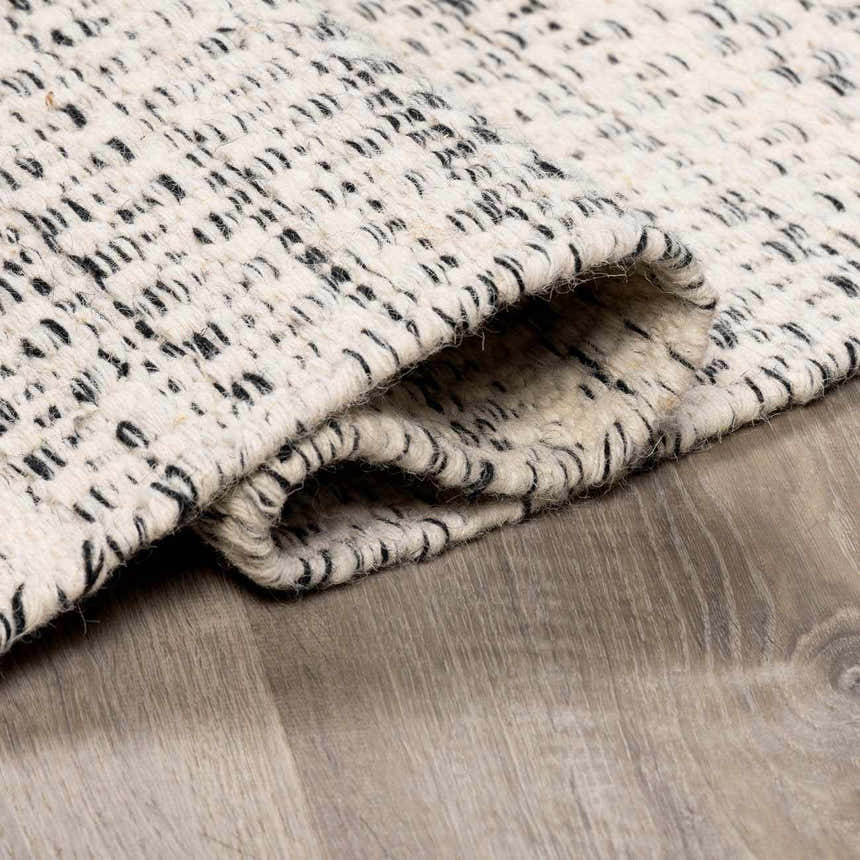 Close-up of the hand-woven Williford Wool Area Rug. Cream wool with black stripes and a visible, textured weave. Fold
