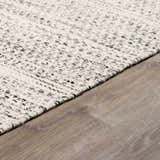 Close-up of the hand-woven Williford Wool Area Rug. Cream rug with black flecks on a wood floor. Transitional style. Corner