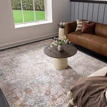 Living room scene with a brown leather sofa and the Witheridge Area Rug in blue, pink, and gray tones. Roomscene-Rectangle
