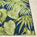 Close up of the Amirah Teal Area Rug showing its green tropical leaf pattern on a navy blue background. Front