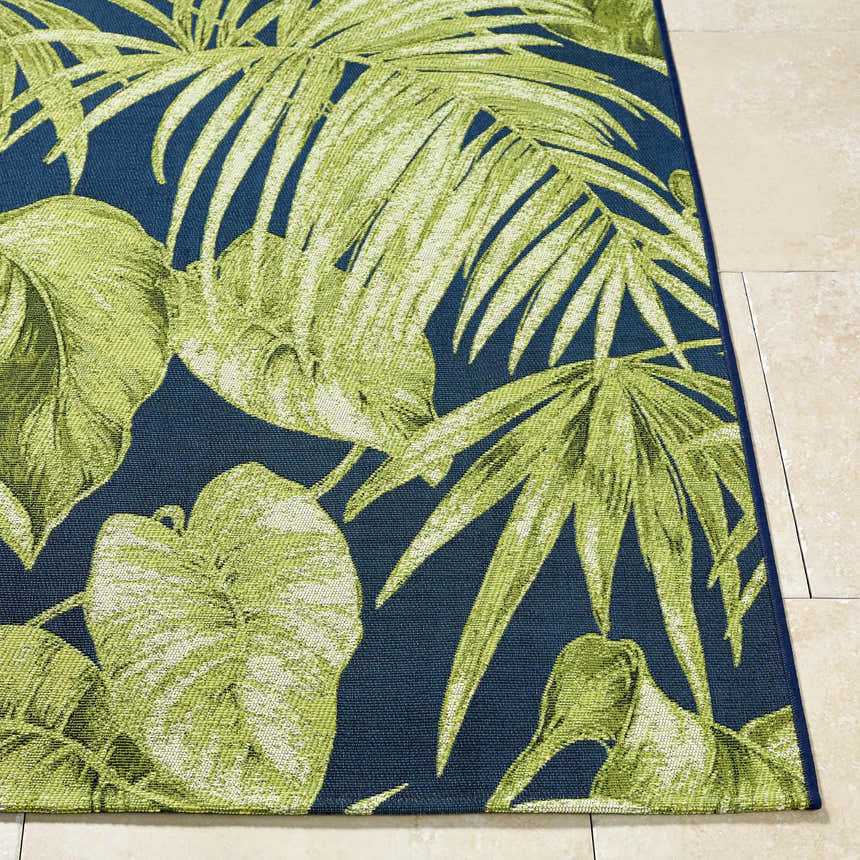 Close up of the Amirah Teal Area Rug showing its green tropical leaf pattern on a navy blue background. Front