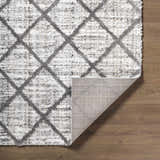 Close-up of the Anuhea Off White Area Rug showing its diamond pattern, plush texture, and backing on a wood floor. Fold