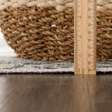 Close-up of Holi-4606 rug edge with ruler showing pile height, next to a woven basket. Black and gold farmhouse style. Pile