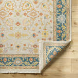 Close-up of the hand-knotted Yenimahalle Premium Rug. Beige wool rug with burnt orange, ice blue, and mustard floral pattern. Fold
