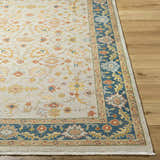 Close-up of the Yenimahalle Premium Rug. Beige rug with burnt orange, ice blue, and mustard floral pattern and teal border. Front