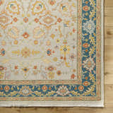 Close-up of the hand-knotted Yenimahalle Premium Rug. Beige rug with burnt orange, ice blue, and mustard floral pattern. Corner