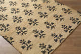 Close-up of the Albina Florentine Jute&Wool Rug. Features a black floral pattern on a tan, hand-woven jute rug. Contemporary style. Corner