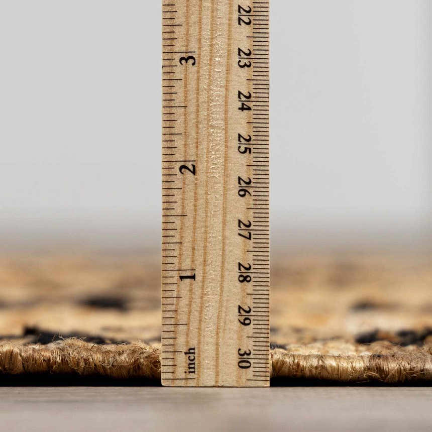 Close-up of Albina Florentine Jute & Wool Rug showing jute texture and pile height using a ruler. Black and brick red colors. Pile
