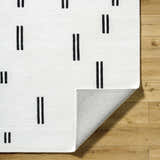 Close-up of the Yitta Ivory Area Rug showing the ivory wool texture and jet black dash pattern on a wood floor. Fold