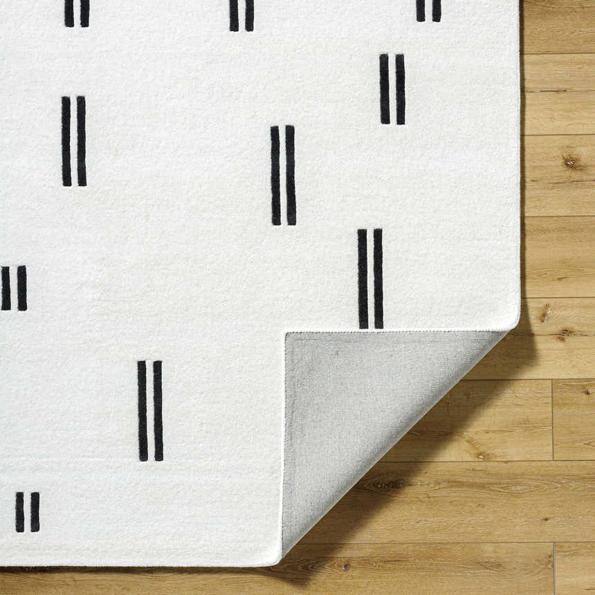 Close-up of the Yitta Ivory Area Rug showing the ivory wool texture and jet black dash pattern on a wood floor. Fold