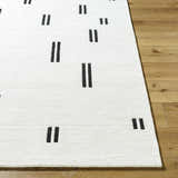 Close-up of the hand-tufted Yitta Ivory Area Rug. Features a contemporary jet black dash pattern on a soft, white wool texture. Front