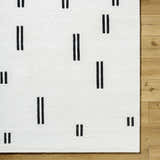 Close-up of the Yitta Ivory Area Rug showing its ivory wool texture and jet black vertical line pattern. Corner