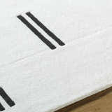 Close-up of the Yitta Ivory Area Rug showing its soft, textured wool and black stripe design. Contemporary style. Texture
