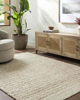 Living room scene with a tan Yaron Area Rug, light wood cabinet, beige chair, and potted plant. Roomscene-Rectangle