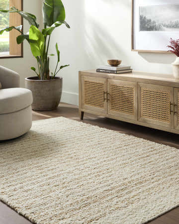 Living room scene with a tan Yaron Area Rug, light wood cabinet, beige chair, and potted plant. Roomscene-Rectangle