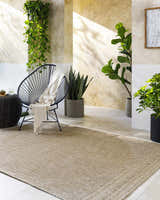 Sunlit patio scene with a tan Yuley Brown Area Rug, modern chair, and potted plants. Roomscene-Rectangle