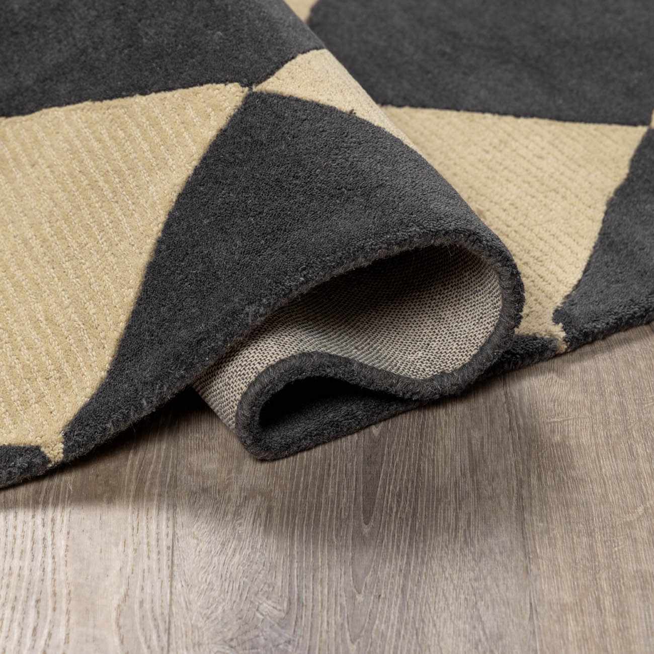 Close-up of the hand-tufted Aradia Charcoal Area Rug showing its wool texture and geometric pattern in charcoal and beige. Fold