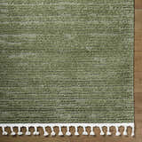 Close-up of the Annily Area Rug. Olive green rug with horizontal stripes and white tassels on a wood floor. Swatch