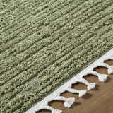 Close-up of the olive green Annily Area Rug showing its textured, ridged design and white braided tassels. Texture