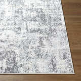 Close up of the Alviva Area Rug showing its charcoal, gray, and ivory abstract pattern and texture on wood flooring. Front